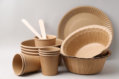 Photo of Set of disposable tableware and green leaves on light grey background, closeup