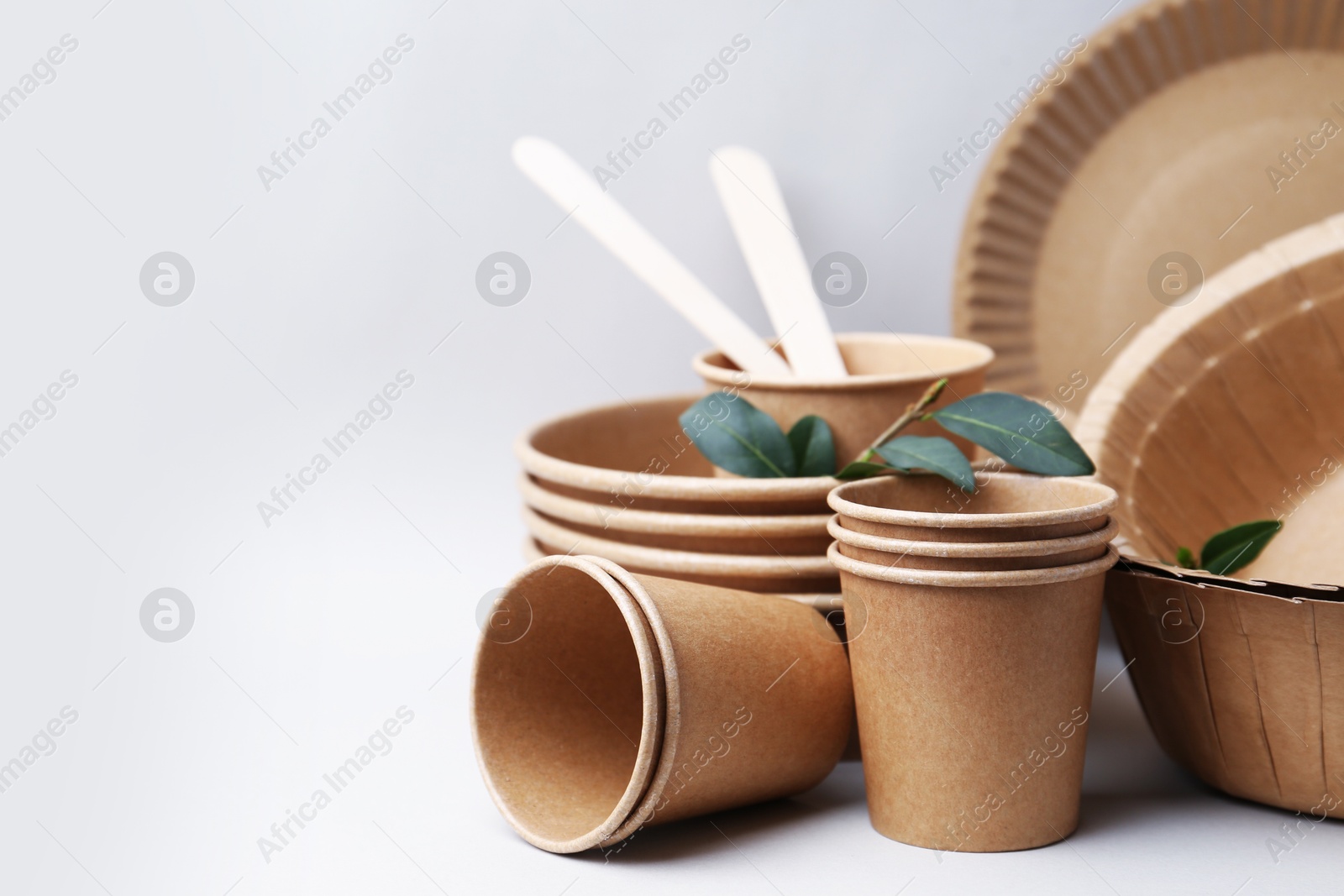 Photo of Set of disposable tableware and green leaves on light grey background, closeup. Space for text
