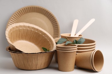 Photo of Set of disposable tableware and green leaves on light grey background, closeup