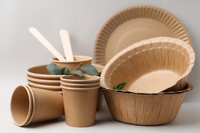 Photo of Set of disposable tableware and green leaves on light grey background, closeup