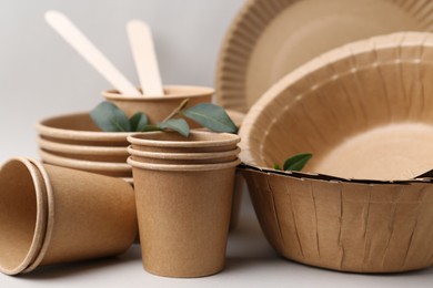 Photo of Set of disposable tableware and green leaves on light grey background, closeup