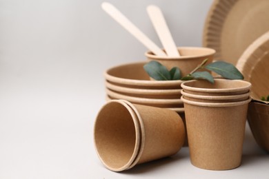 Photo of Set of disposable tableware and green leaves on light grey background, closeup. Space for text