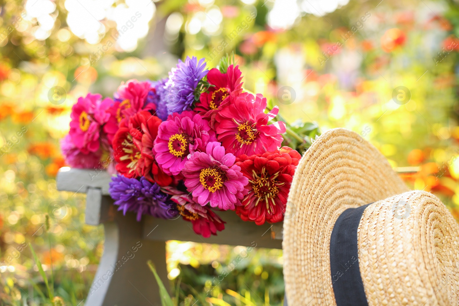 Photo of Bouquet of flowers on stool and wicker hat outdoors, closeup