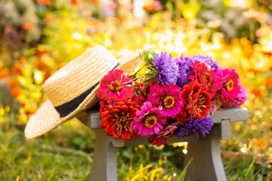 Photo of Bouquet of flowers and wicker hat on stool outdoors, closeup