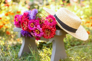 Photo of Bouquet of flowers and wicker hat on stool outdoors, closeup