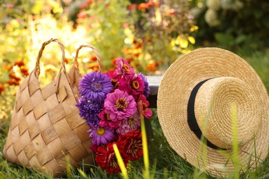 Photo of Bouquet of flowers in bag and wicker hat on green grass outdoors
