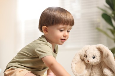 Photo of Cute little boy playing with his toy bunny indoors