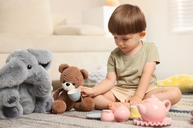 Photo of Cute little boy playing tea party with his toys indoors