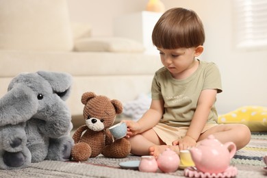 Photo of Cute little boy playing tea party with his toys indoors