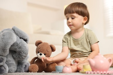 Photo of Cute little boy playing tea party with his toys indoors