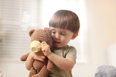 Photo of Cute little boy playing tea party with his toy bear indoors