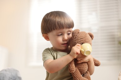 Photo of Cute little boy playing tea party with his toy bear indoors