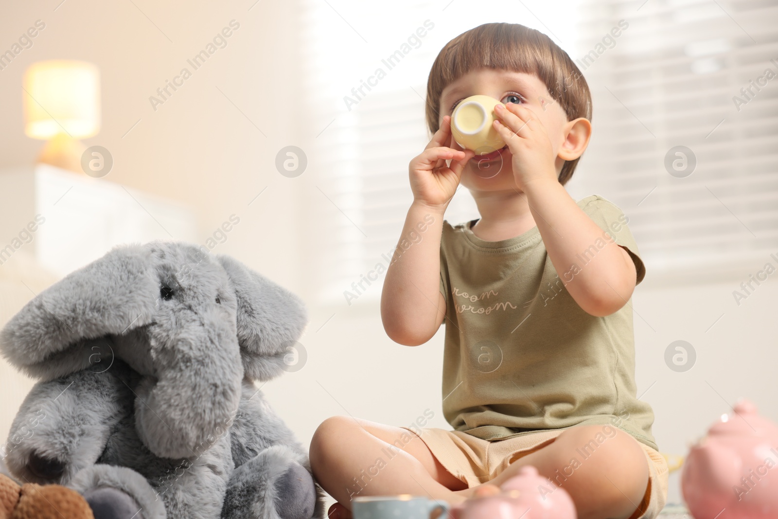 Photo of Cute little boy playing tea party with his toy elephant indoors