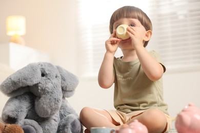 Photo of Cute little boy playing tea party with his toy elephant indoors