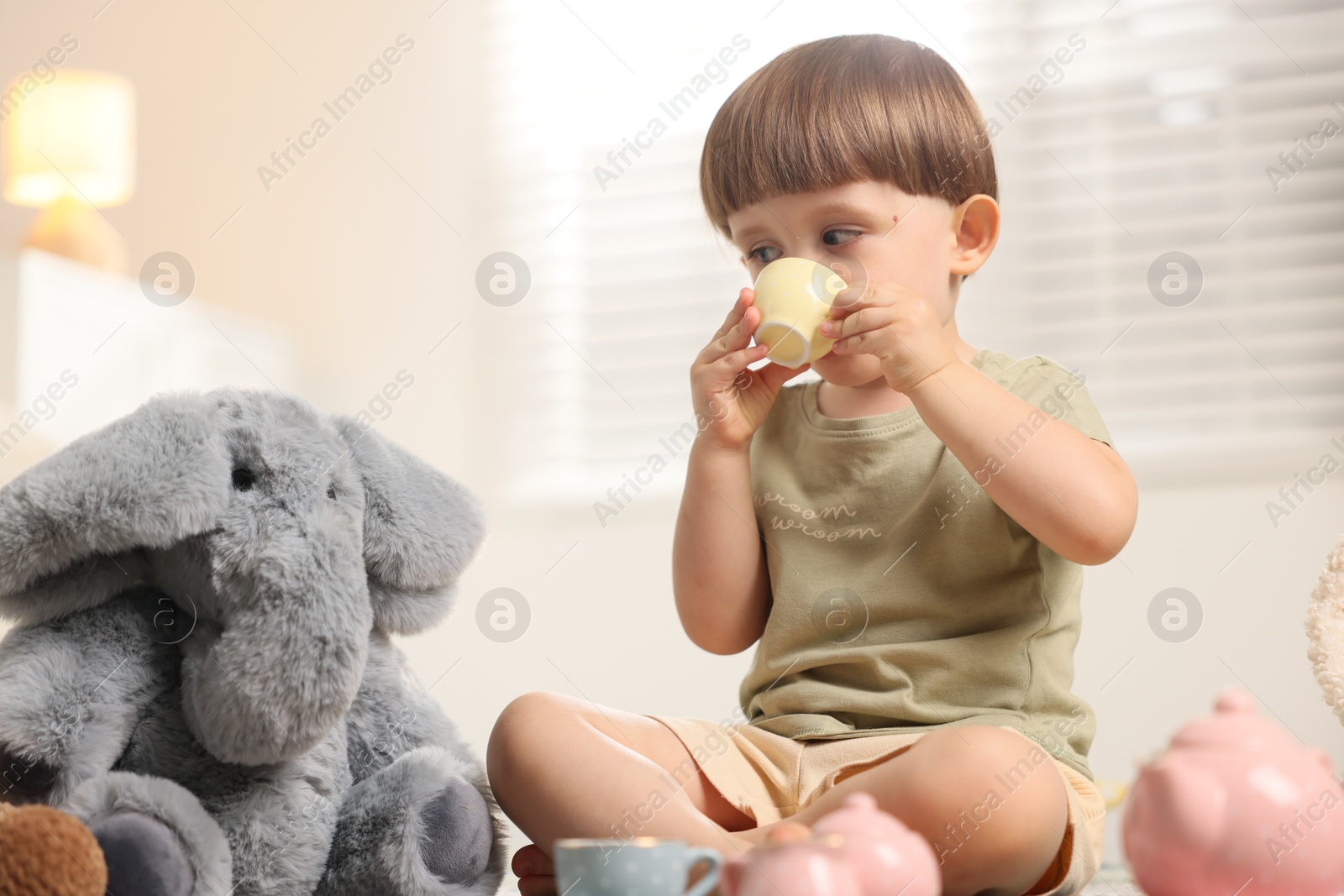 Photo of Cute little boy playing tea party with his toy elephant indoors