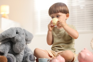 Photo of Cute little boy playing tea party with his toy elephant indoors