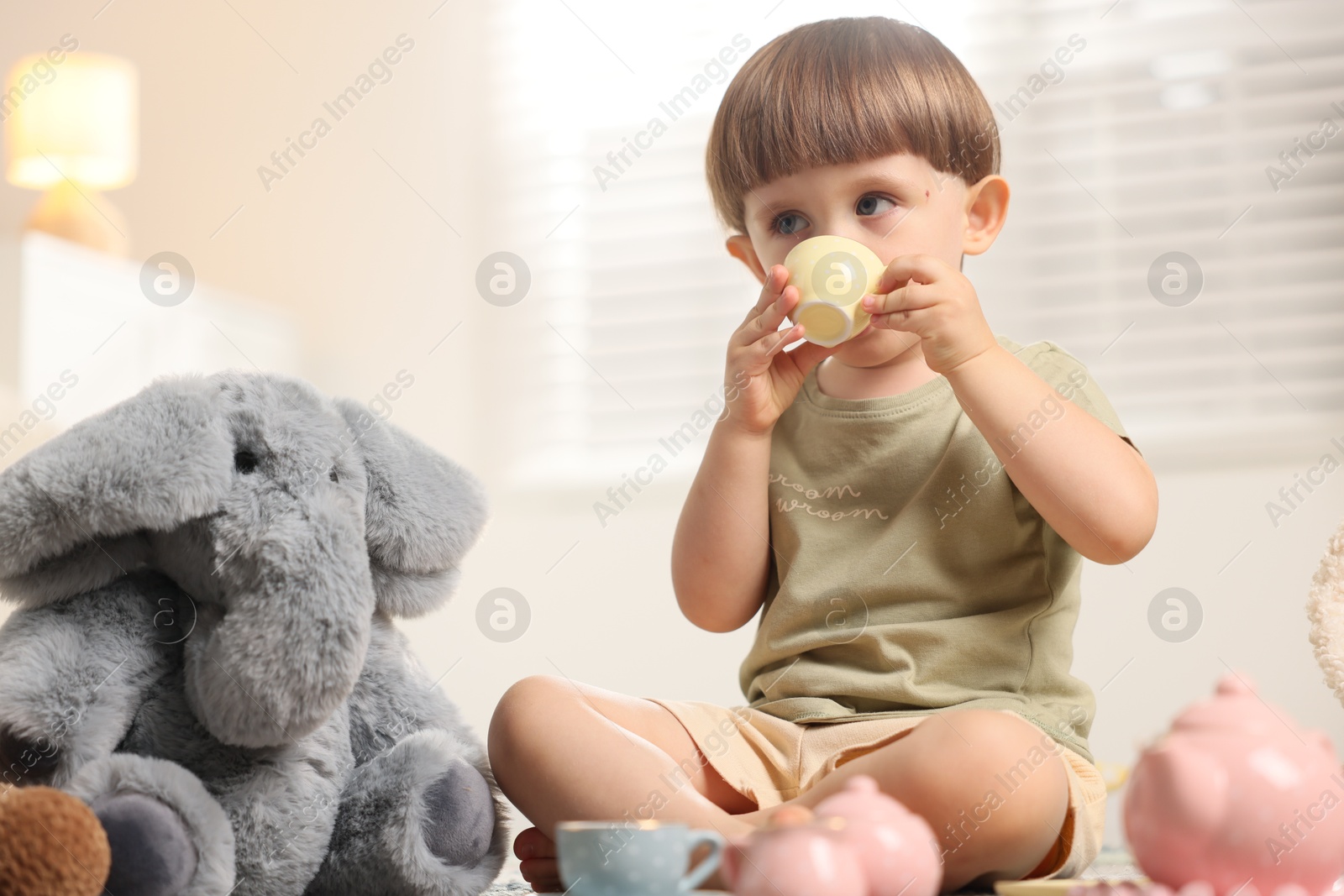 Photo of Cute little boy playing tea party with his toy elephant indoors