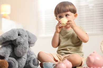 Photo of Cute little boy playing tea party with his toy elephant indoors
