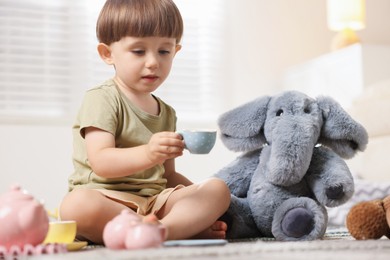 Photo of Cute little boy playing tea party with his toy elephant indoors
