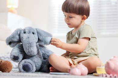Photo of Cute little boy playing tea party with his toy elephant indoors