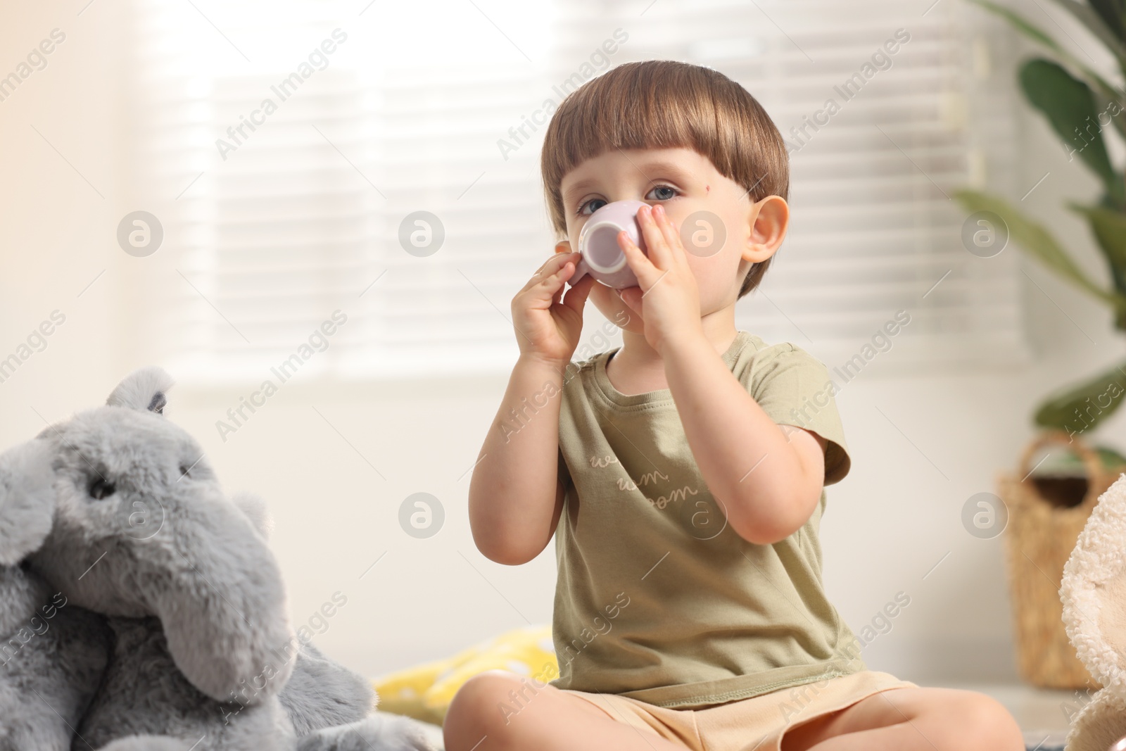 Photo of Cute little boy playing tea party with his toy elephant indoors. Space for text