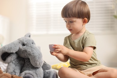 Photo of Cute little boy playing tea party with his toy elephant indoors