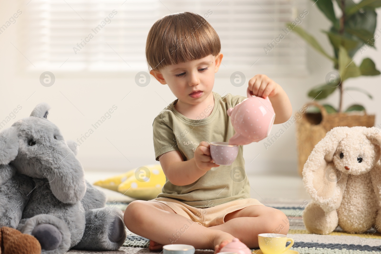 Photo of Cute little boy playing tea party with his toys indoors