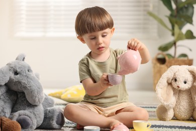 Photo of Cute little boy playing tea party with his toys indoors