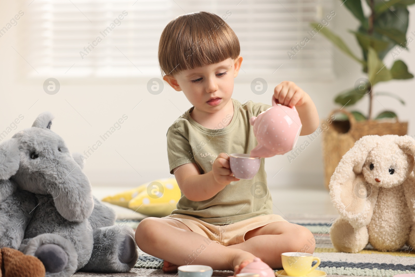 Photo of Cute little boy playing tea party with his toys indoors