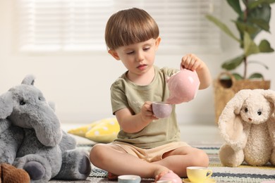 Photo of Cute little boy playing tea party with his toys indoors