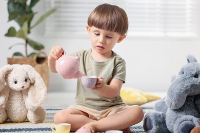 Photo of Cute little boy playing tea party with his toys indoors