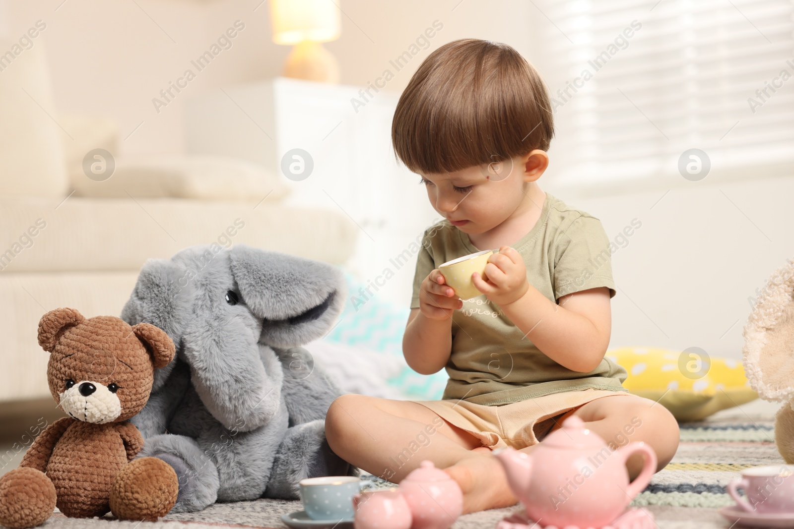 Photo of Cute little boy playing tea party with his toys indoors
