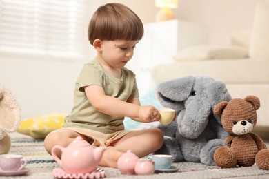 Photo of Cute little boy playing tea party with his toys indoors
