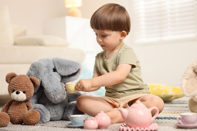 Photo of Cute little boy playing tea party with his toys indoors