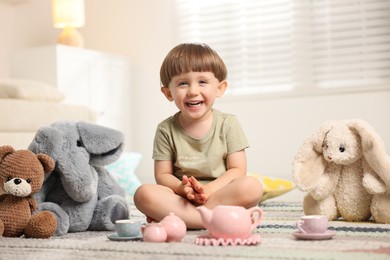 Photo of Cute little boy playing tea party with his toys indoors