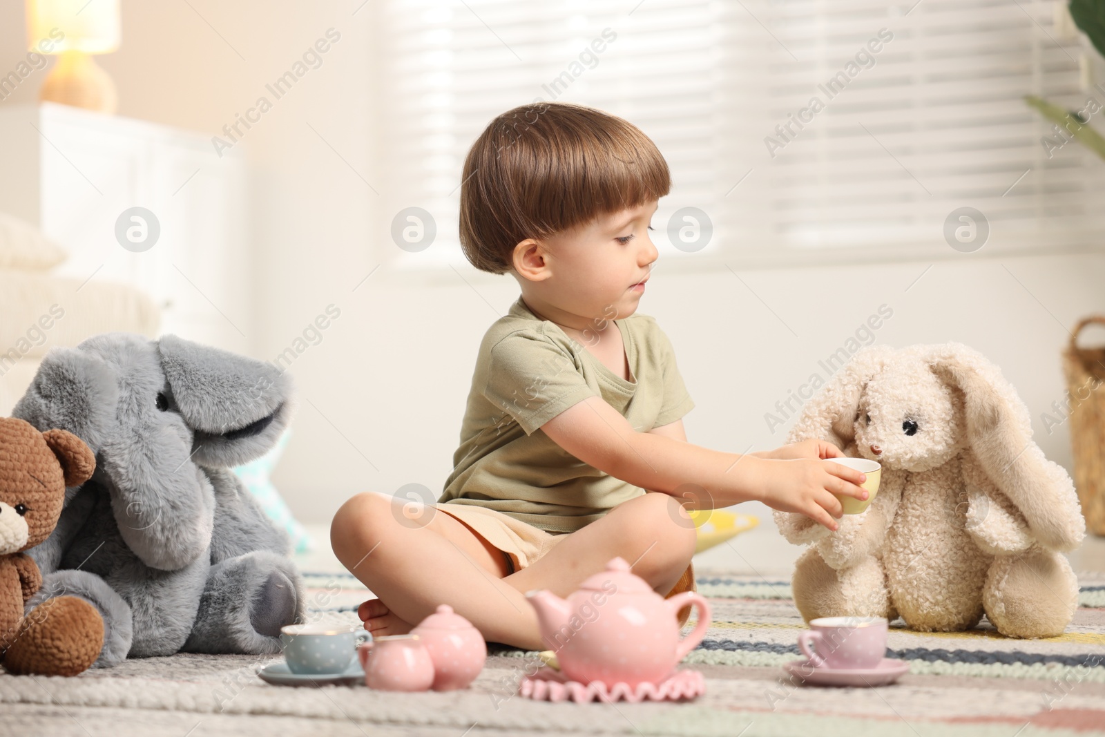 Photo of Cute little boy playing tea party with his toys indoors