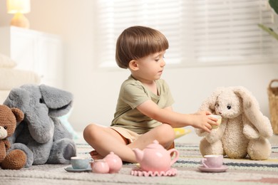 Photo of Cute little boy playing tea party with his toys indoors