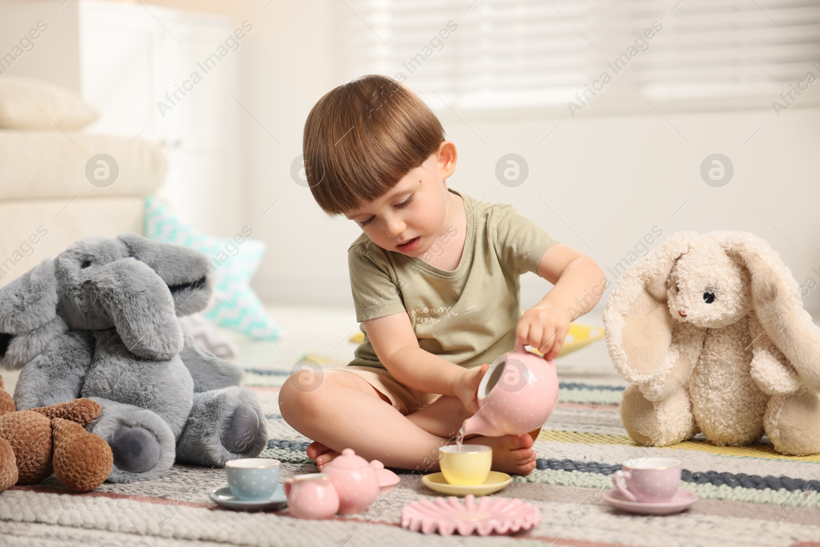 Photo of Cute little boy playing tea party with his toys indoors