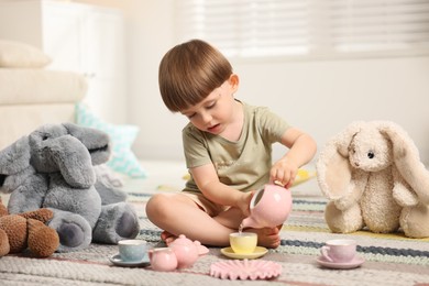 Photo of Cute little boy playing tea party with his toys indoors