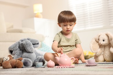Photo of Cute little boy playing tea party with his toys indoors