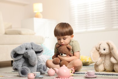 Photo of Cute little boy playing tea party with his toys indoors
