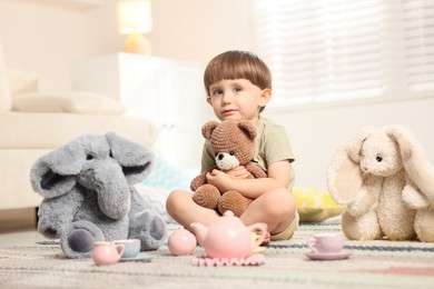 Photo of Cute little boy playing tea party with his toys indoors