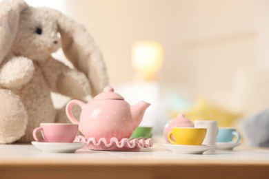 Photo of Tea set and stuffed bunny on white table indoors, closeup with space for text. Child's toy