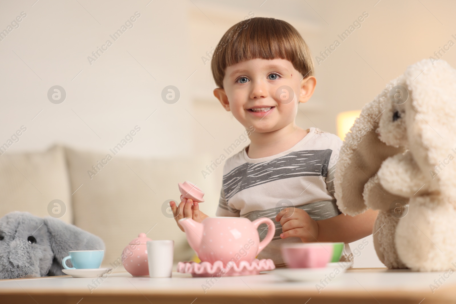 Photo of Cute little boy playing tea party with his toys at table indoors. Space for text