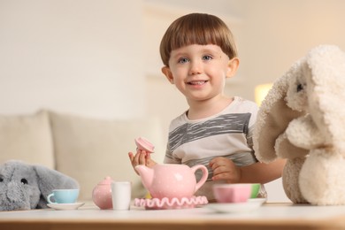 Photo of Cute little boy playing tea party with his toys at table indoors. Space for text