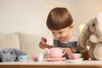 Photo of Cute little boy playing tea party with his toys at table indoors. Space for text