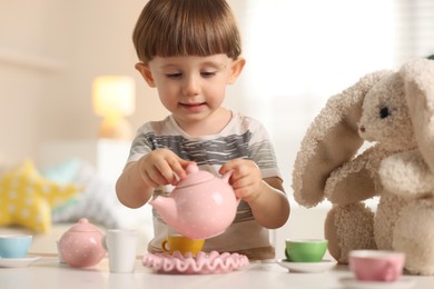 Photo of Cute little boy playing tea party with his toy bunny at table indoors