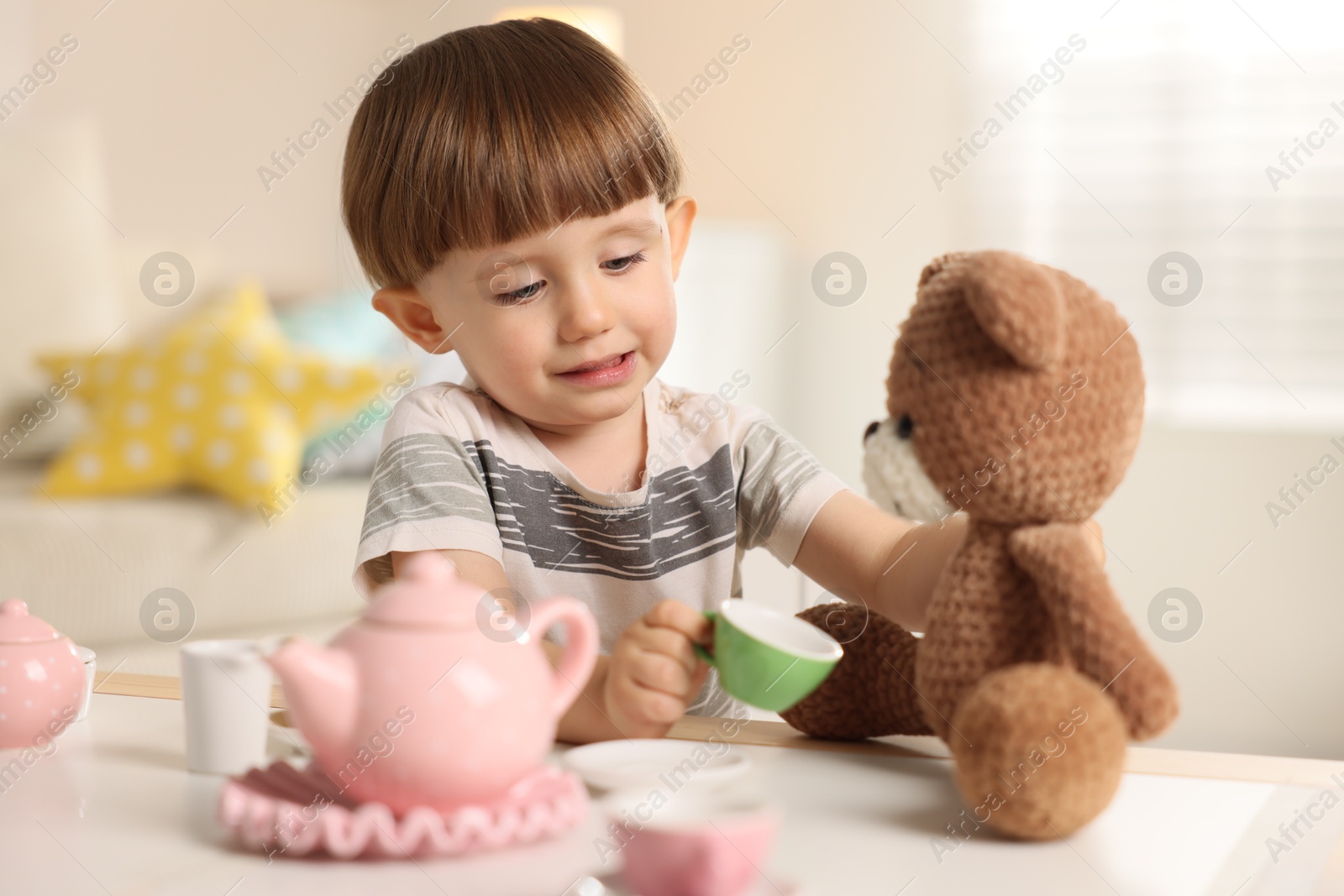 Photo of Cute little boy playing tea party with his toy bear at table indoors