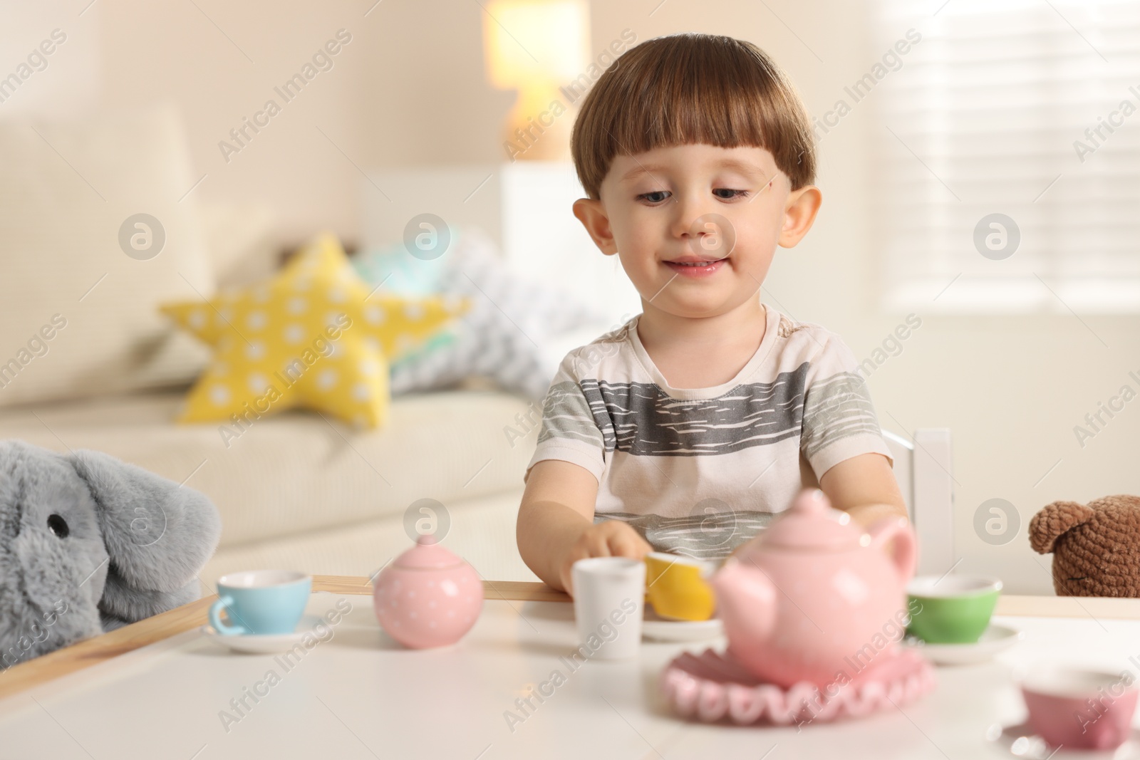 Photo of Cute little boy playing tea party with his toy elephant at table indoors. Space for text