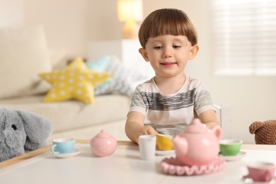 Photo of Cute little boy playing tea party with his toy elephant at table indoors. Space for text